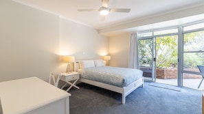 A bedroom with a bed, bedside lamps, a desk, and a sliding glass door leading to an outdoor area. - Albacore 1/12-14 Ondine Close, Nelson Bay NSW 2315 (Nelson Bay)