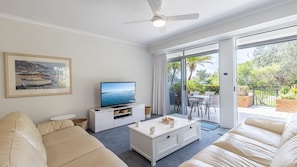 A modern living room with a flat-screen TV, a white coffee table, and a beige sofa. - Albacore 1/12-14 Ondine Close, Nelson Bay NSW 2315 (Nelson Bay)