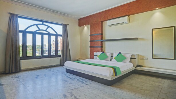 A hotel room with a bed, a window with curtains, an air conditioning unit, and a view of buildings outside. - Treebo Trend Jai Mahal (Udaipur)
