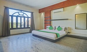 A hotel room with a bed, a window with curtains, an air conditioning unit, and a view of buildings outside. - Treebo Trend Jai Mahal (Udaipur)