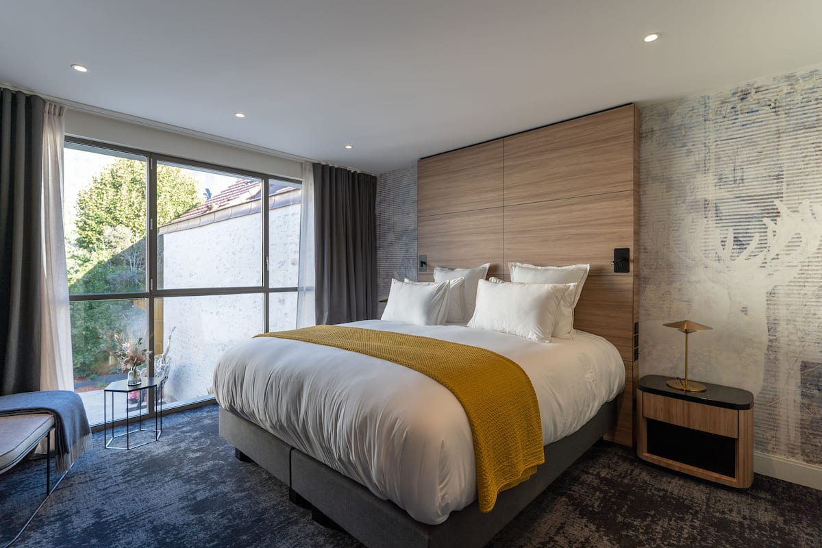 A modern bedroom with a large bed, a bedside table, and a view of the outdoors.