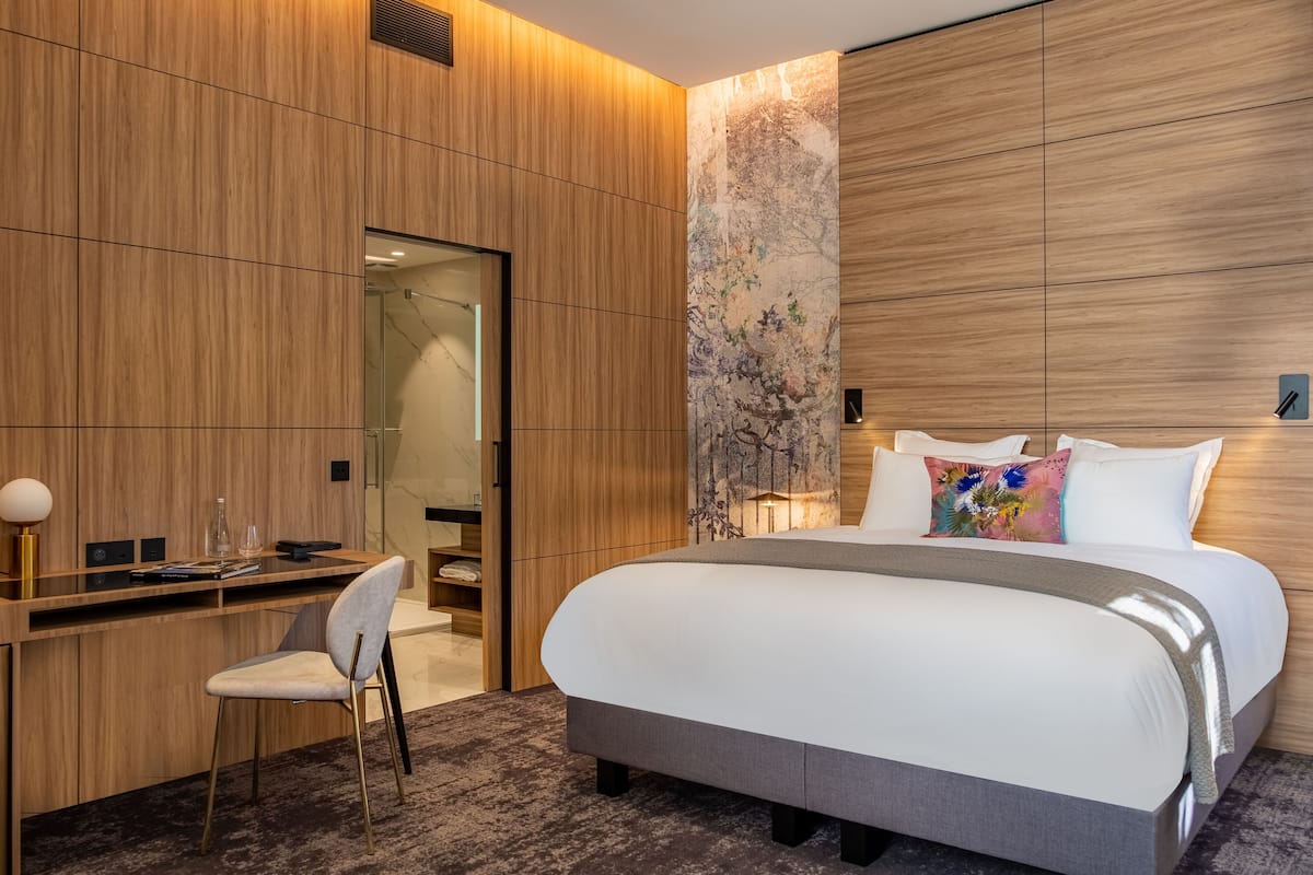 A modern hotel room with a large bed, a desk with a chair, and a large mirror.
