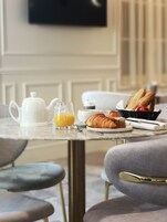 Uma mesa de café da manhã com croissants, suco de laranja, um bule e uma cesta de pão.