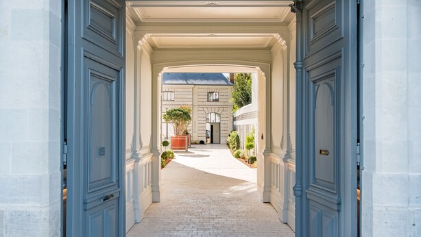 A corridor with a brick floor leading to a building with a blue roof. - Les Trésorières (Tours)