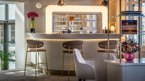 A modern bar area with a white countertop, three bar stools, and a seating area with a white armchair. - Les Trésorières (Tours)