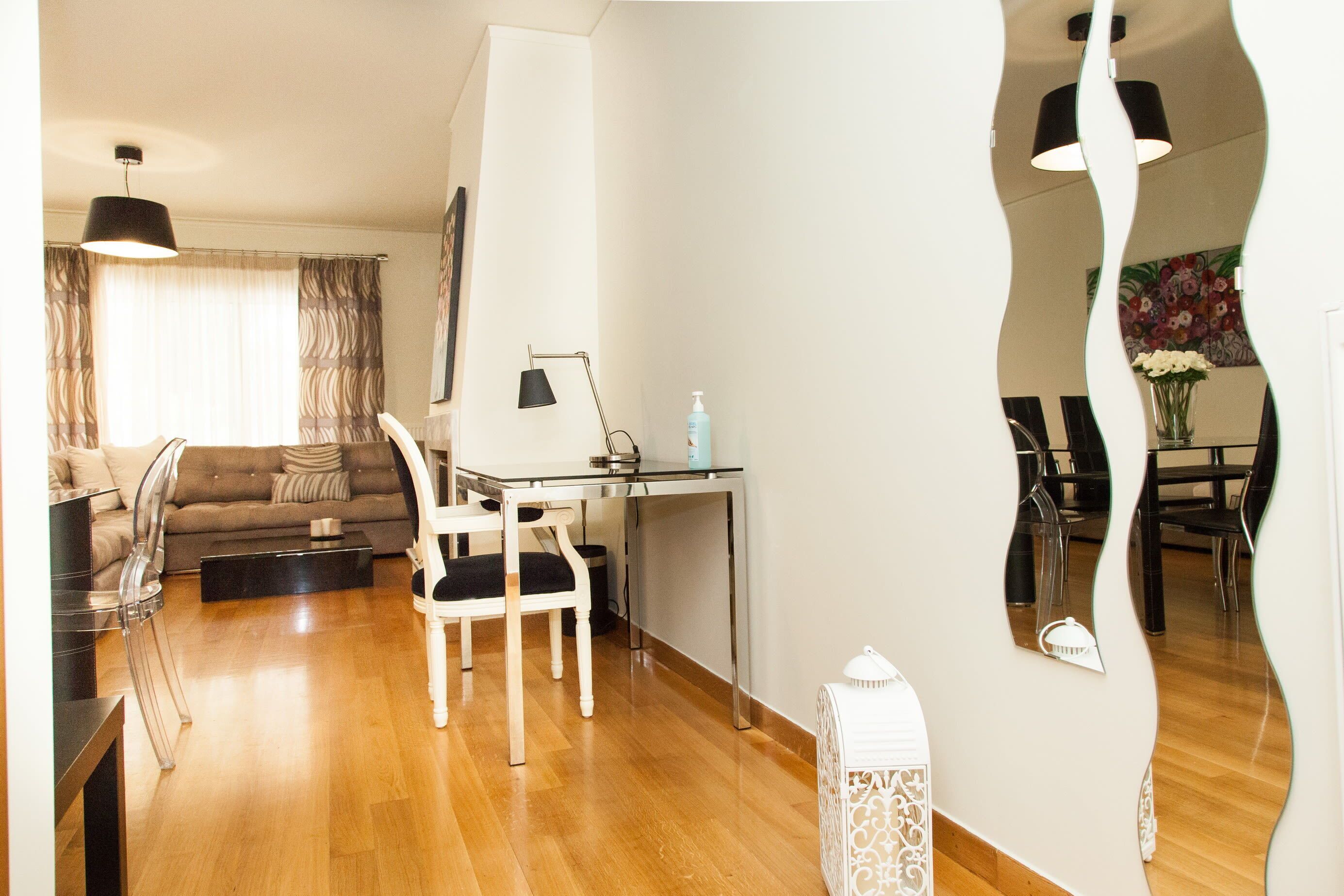 Ein modernes Wohnzimmer mit einer Couch, einem Esstisch und Stühlen. Eine Lampe, ein kleiner Tisch mit einer Flasche und ein dekoratives Objekt sind auf dem Boden zu sehen.