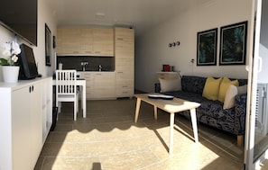 Ein kompakter Wohnbereich mit Küchenzeile, Essplatz und einer Couch mit Kissen.