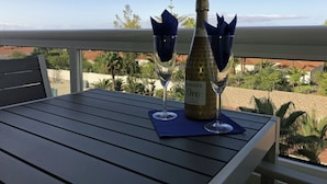 Une table avec une bouteille de vin et deux verres, placée sur un balcon donnant sur un quartier résidentiel.