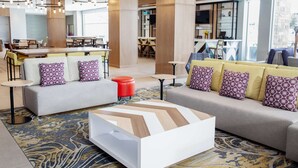 A modern hotel lobby with a central seating area, a bar, and a dining area.