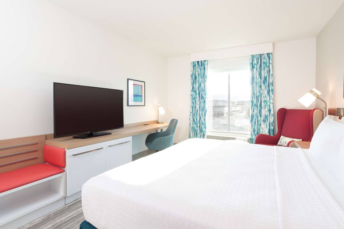 A hotel room with a bed, a desk with a chair, a television, and a window with curtains.