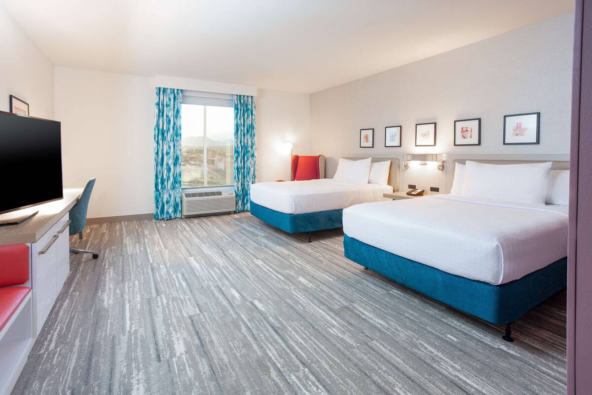 A hotel room with two beds, a desk, a TV, and a window with curtains.