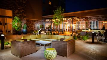 Relax on the patio with a sofa, armchairs, and a small table, surrounded by lush greenery and twinkling lights.