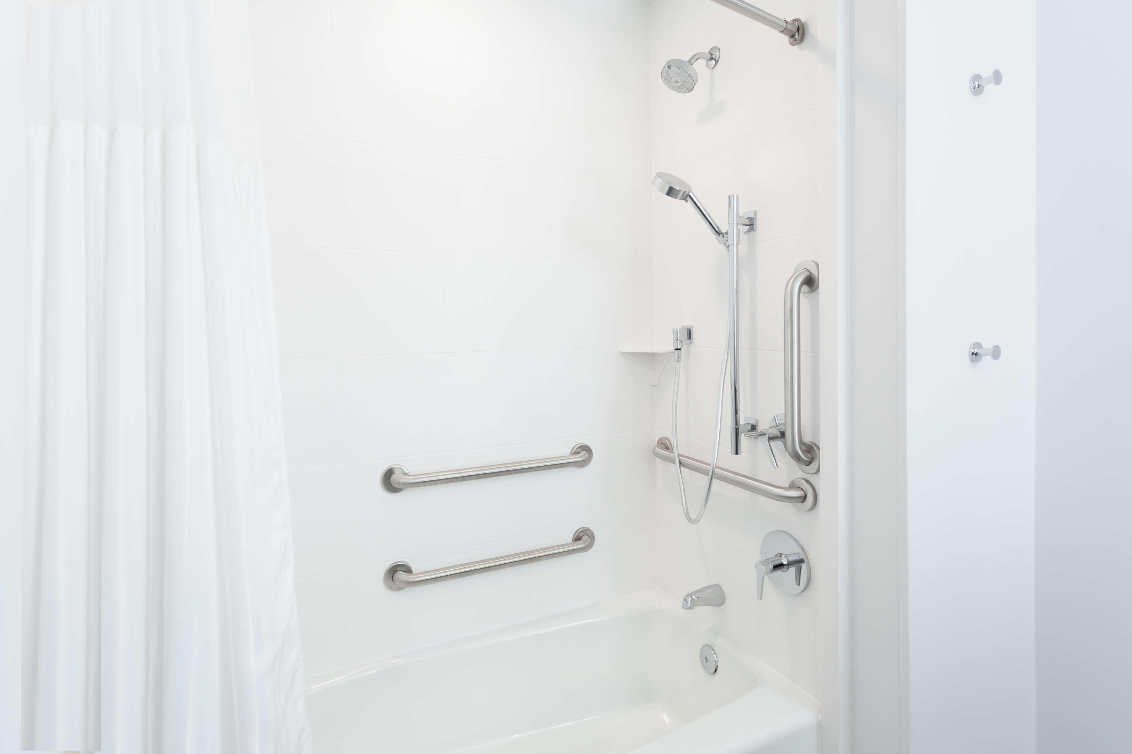 Une salle de bain moderne équipée d’une baignoire, d’une douche et de barres d’appui.