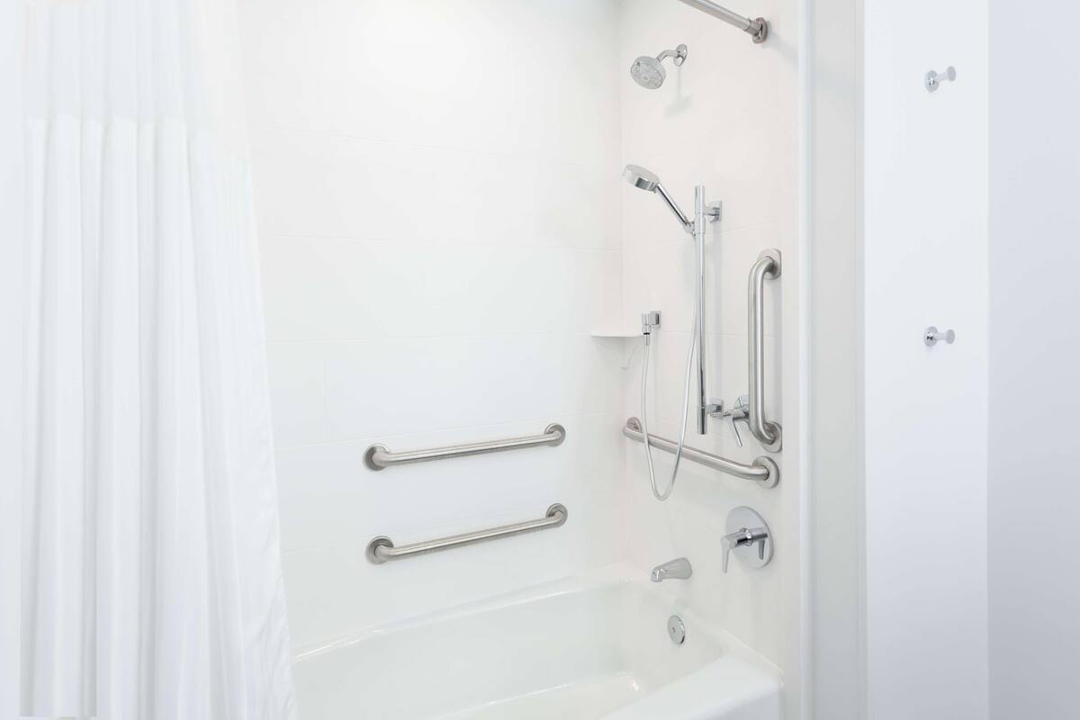 A white bathroom with a bathtub, grab bars, and a showerhead.