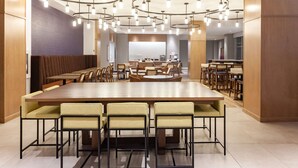 A spacious dining area with a long wooden table surrounded by chairs, a modern chandelier, and a seating area with cushioned benches.