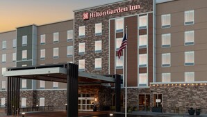 A Hilton Garden Inn with a brick facade, multiple windows, and an American flag.