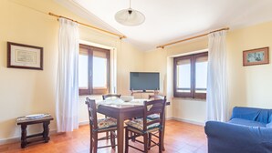 A dining area with a table and chairs, a television, and a sofa.