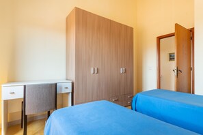 A bedroom with a wooden wardrobe, a desk with a chair, and two beds with blue bedding. - Vacation Home da Placida "S'Archittu" (Suni)