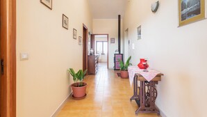 A hallway with potted plants, a table with a red vase, and framed pictures on the walls.