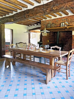 A wooden dining table with benches, hanging pendant lights, a brick fireplace, and a tiled floor.