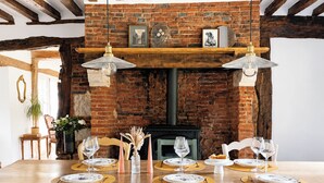 Un espace repas agrémenté d’une cheminée en briques, de poutres en bois et d’une longue table dressée pour le repas.