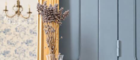 A marble fireplace with a vase of dried flowers, a framed mirror, and a chandelier in the background.