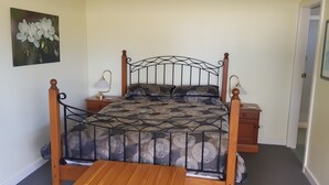 Un lit simple avec un cadre en métal, une tête de lit en bois et une couvre-lit à motifs. Il y a deux tables de chevet avec des lampes, et une porte sur la droite.