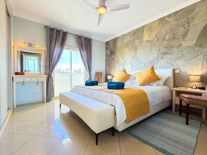 A bedroom with a bed, bedside table, lamp, and a view through the window.