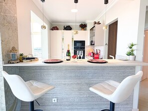 A modern kitchen with a bar area, white bar stools, and a view of the city.