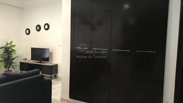 A modern living room with a black wardrobe, a flat-screen TV, a sofa, and a potted plant. - Superb Mont Carlo Hamam Sousse vacation apartment (Hammam Sousse)