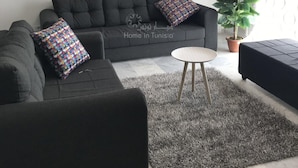 A living room with a dark grey sofa, two patterned cushions, a small round table, and a potted plant. - Superb Mont Carlo Hamam Sousse vacation apartment (Hammam Sousse)