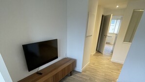 Ein modernes Wohnzimmer mit einem Flachbildfernseher auf einer Holzkonsolen, hellem Holzboden und Blick in den angrenzenden Küchenbereich.