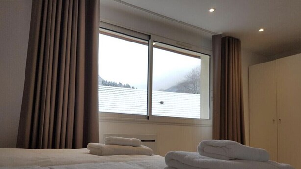 Ein Hotelzimmer mit einem großen Bett, einem Fenster mit Vorhängen und Blick auf einen See.