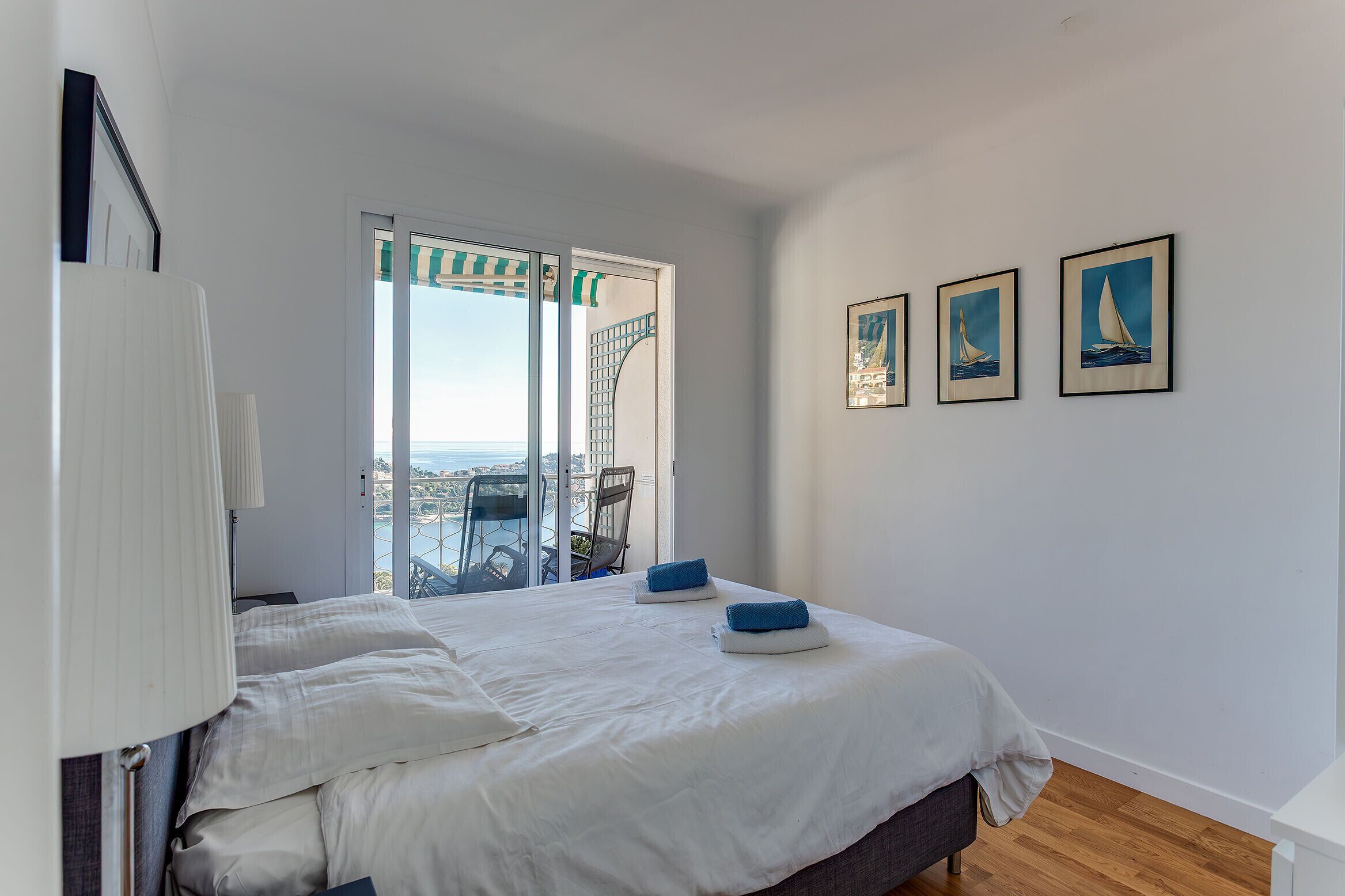 A bedroom with a bed, a view of the city, and three framed pictures on the wall.