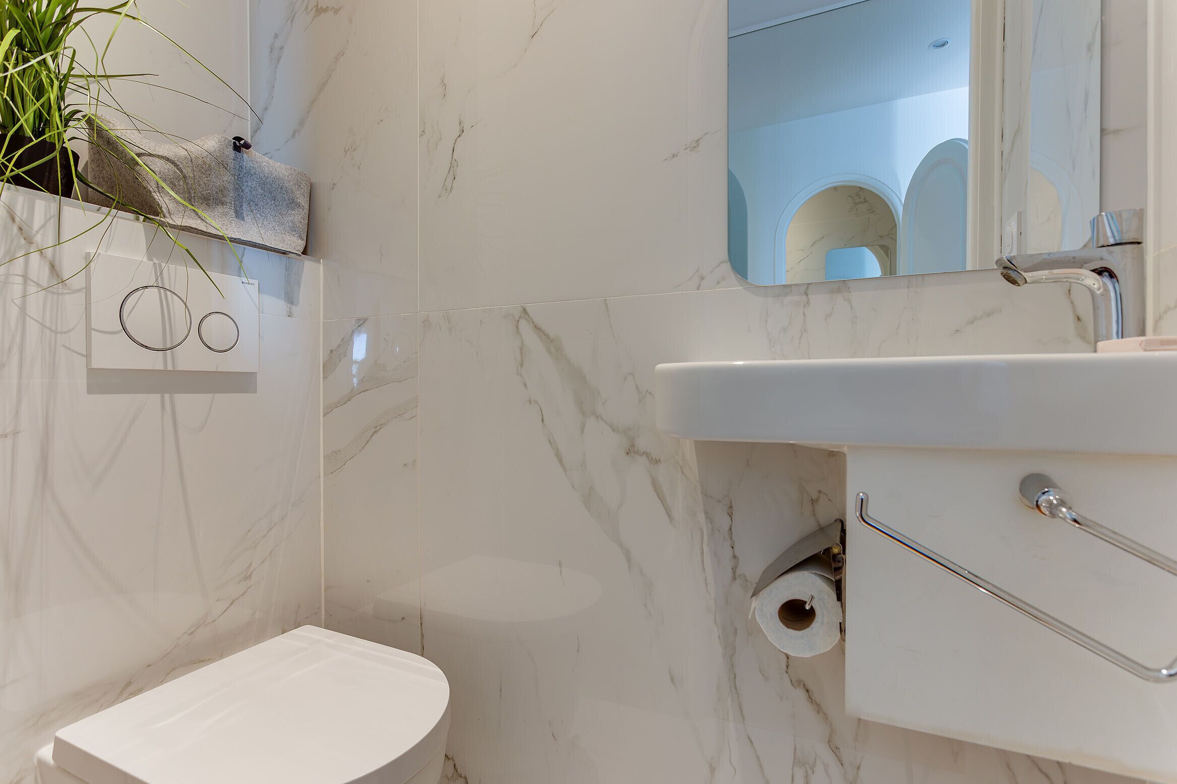 A bathroom with a marble wall, a white sink, a toilet, and a mirror.