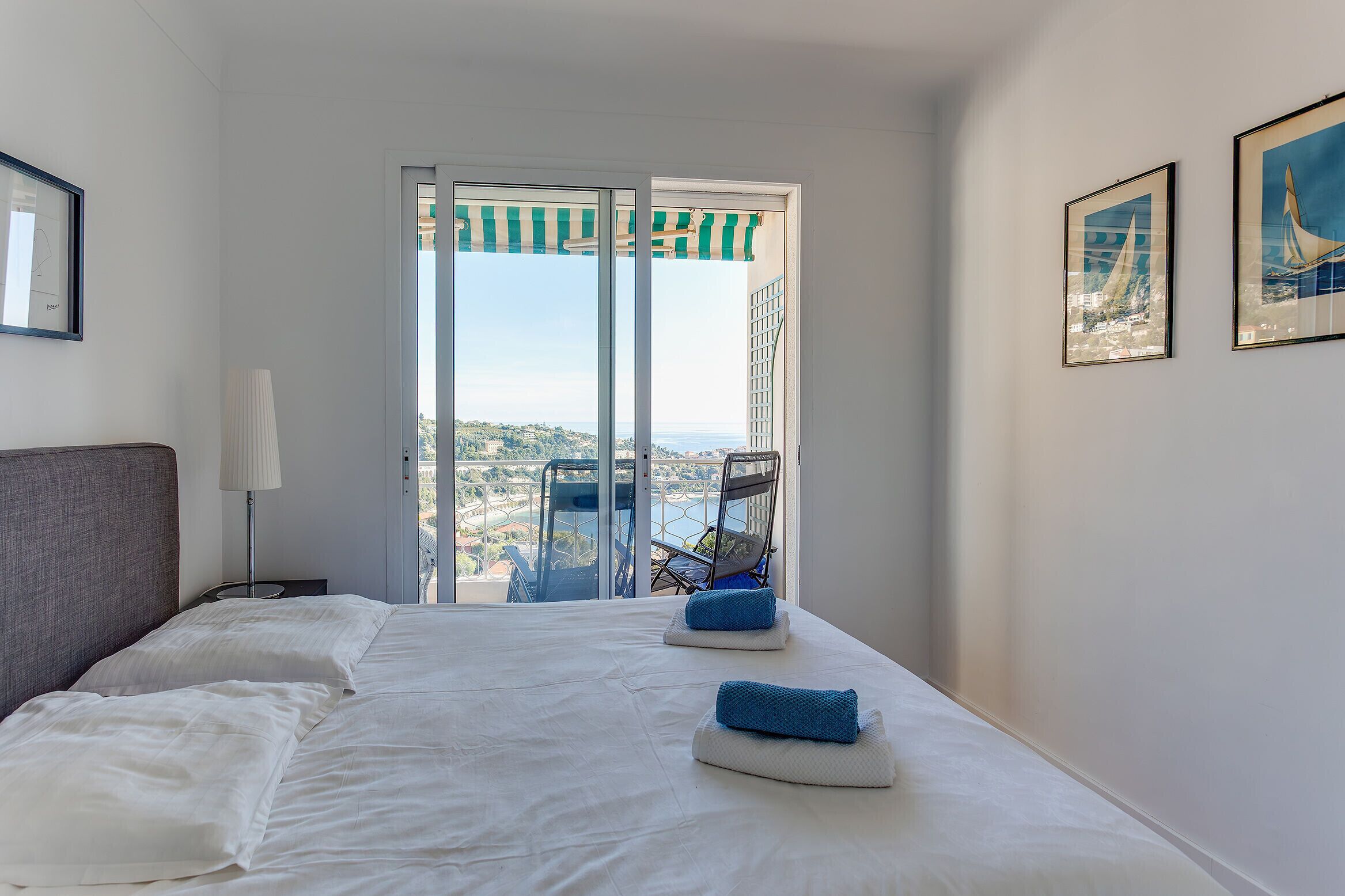 Ein Hotelzimmer mit Bett, einem Sessel und Blick auf die Stadt durch eine Glastür.