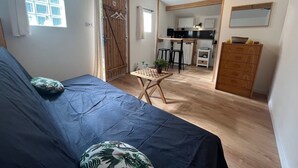 Une pièce confortable avec un lit, une petite table et un coin cuisine visible à travers une porte ouverte.