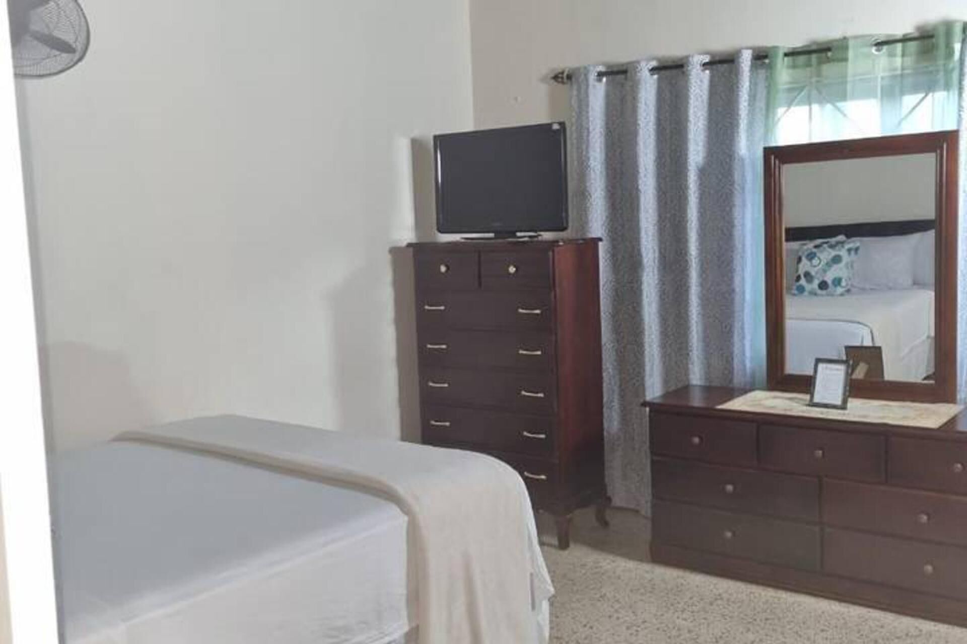 A bedroom with a bed, a dresser, a television on top of the dresser, and a mirror on the dresser.