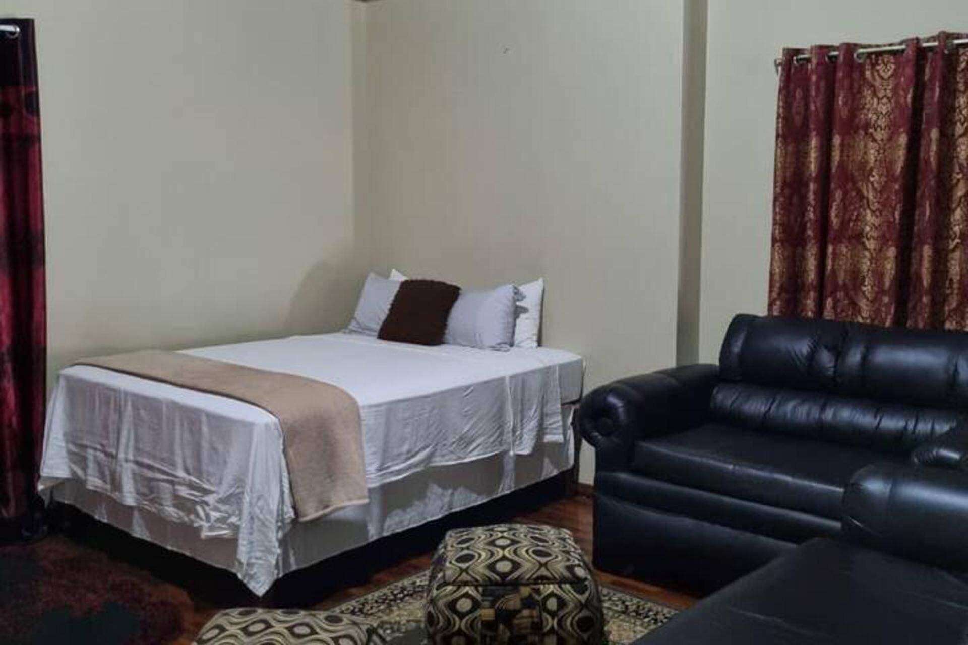 A bedroom with a bed, a black leather sofa, and a patterned ottoman.