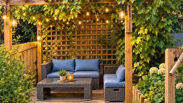 An outdoor patio with a wooden pergola, string lights, a cushioned sofa, and a coffee table.