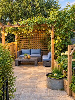 Un patio al aire libre con una pérgola de madera, luces colgantes, un sofá con cojines y una mesa de centro.
