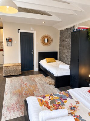 Un dormitorio con cama, armario, mesita de noche, lámpara colgante, pared con estampado y una puerta.