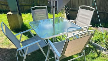 Une table avec un plateau en verre, quatre chaises, une clôture en bois et une cour gazonnée.