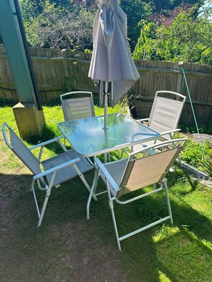Une table avec un plateau en verre, quatre chaises, une clôture en bois et une cour gazonnée.