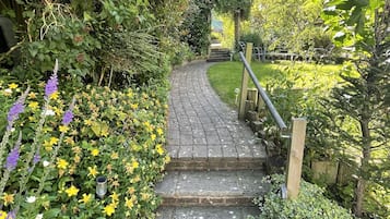 Un chemin de pierres qui traverse un jardin où l’on trouve différentes plantes et fleurs.