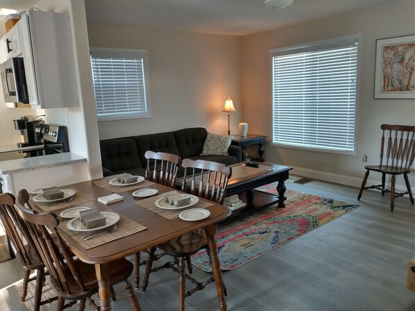 A dining area with a wooden table set for four, a black sofa, and a coffee table.