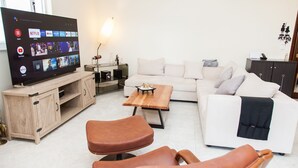 A living room with a TV displaying streaming services, a white sofa, a wooden coffee table, and two leather chairs. - Modern apt.with sea view in Glyfada (Glyfada)