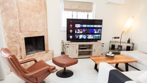 A modern living room with a fireplace, a leather armchair, a sofa, a coffee table, and a flat-screen TV displaying various streaming services. - Modern apt.with sea view in Glyfada (Glyfada)