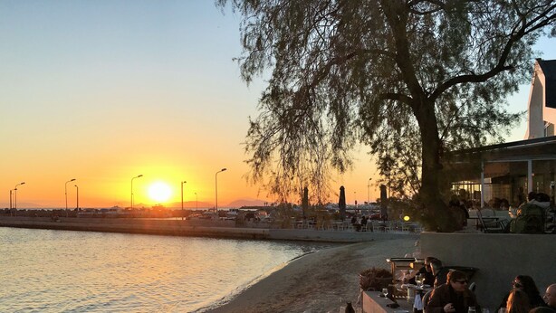 A waterfront restaurant with outdoor seating, a view of the sunset, and a stone wall separating the dining area from the water. - Modern apt.with sea view in Glyfada (Glyfada)