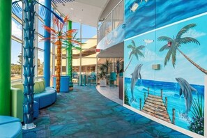 Un vaste espace intérieur agrémenté d’une fresque représentant des dauphins, d’une jetée en bois, de coins salon et d’un escalier aux couleurs bleue et verte.